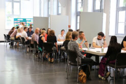 Personen sitzen an Gruppenarbeitstischen.