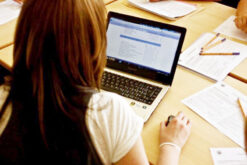 Junge Frau sitzt am Tisch und füllt eine Umfrage am Laptop aus.
