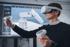 Person mit VR-Brille und VR-Controllern steht vor einem Smartboard.