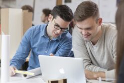 Zwei junge Männer sitzen vor einem Laptop und besprechen etwas.