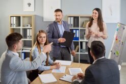 Mehrere Personen stehen um einen Tisch im Büro herum und besprechen etwas.