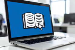 Aufgeklappter Laptop, auf dessen Bildschirm der Curser der Maus auf einem aufgeschlagenen Buch liegt.