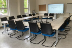 Ein heller Workshopraum mit einem Smartboard und u-förmig angeordneten Tische mit Stühlen.