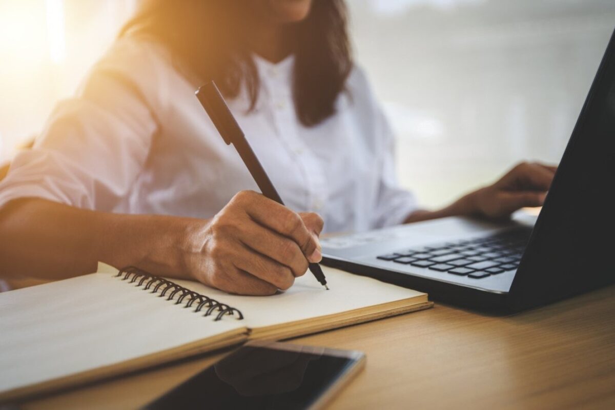 Eine Person am Laptop, die sich per Hand Notizen macht