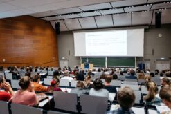 Vortrag einer Lehrperson im Hörsaal, bei dem Studierende zuhören.