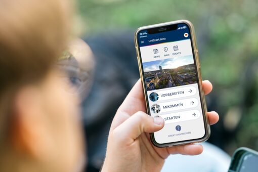 Großaufnahme eines Smartphones, das die Startseite der App UniStartjena anzeigt.