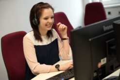 Frau sitzt mit Headset vor einem Monitor und gibt Support.